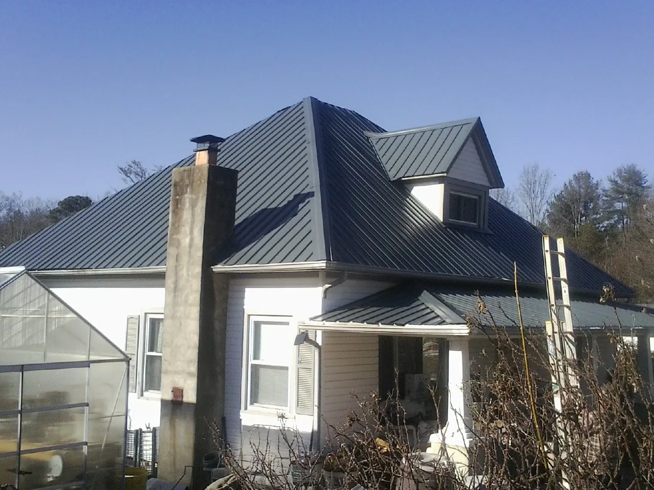 Dark blue standing seam metal roof on a white farmhouse with dormer — Slate & Tile Roof Repair by Roofing Brothers in Port Washington