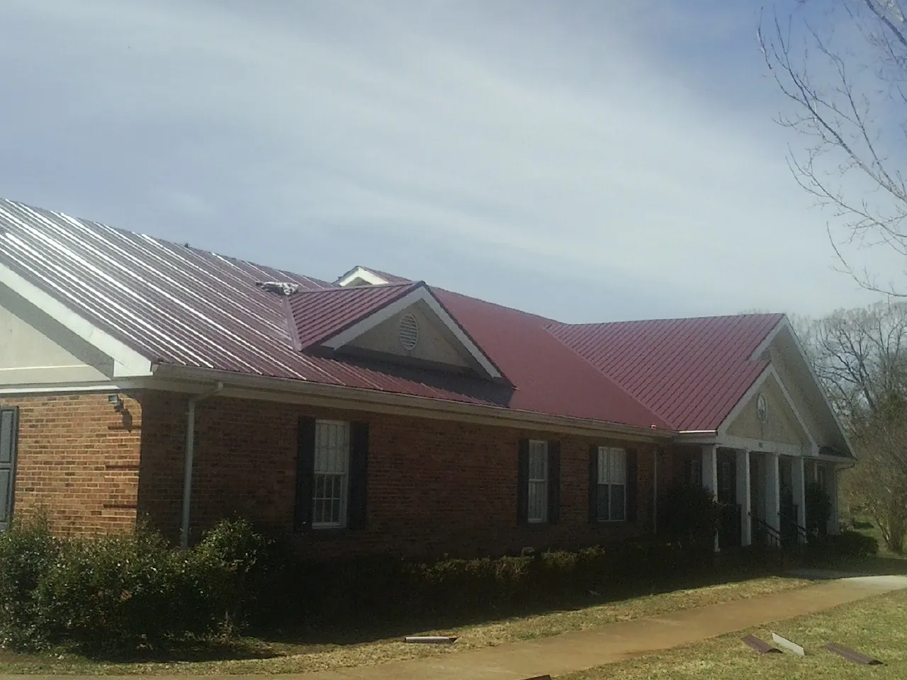 Red metal roof with gabled entries on a long brick building, from a Hail Damage Roof Repair job in Port Washington